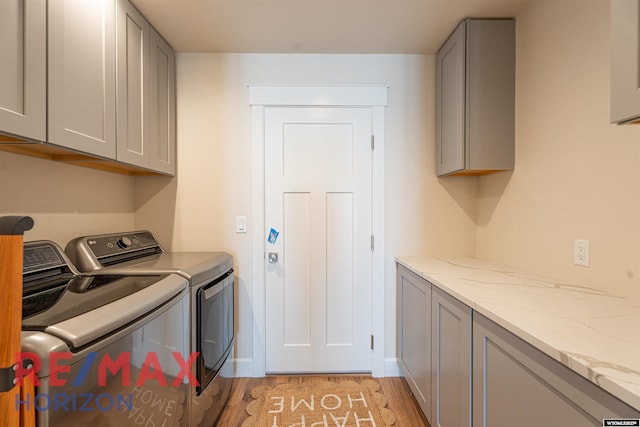 laundry area with cabinet space, light wood-type flooring, washing machine and clothes dryer, and baseboards
