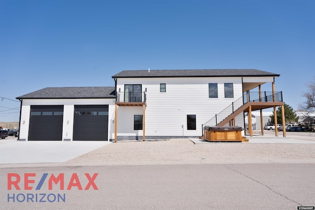 exterior space featuring driveway, a hot tub, a balcony, and a garage