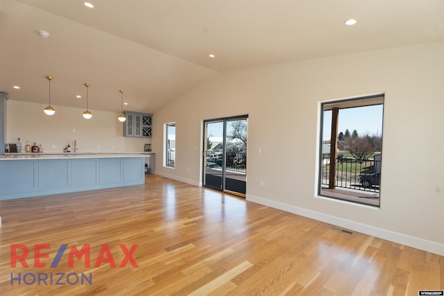 unfurnished living room with wet bar, vaulted ceiling, visible vents, and light wood-type flooring