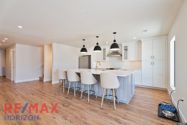 kitchen with white cabinets, light countertops, visible vents, freestanding refrigerator, and a kitchen island with sink