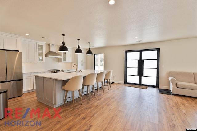 kitchen featuring wall chimney exhaust hood, a kitchen island with sink, white cabinets, open floor plan, and appliances with stainless steel finishes