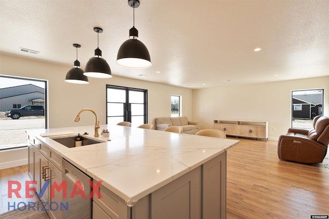 kitchen with stainless steel dishwasher, a sink, open floor plan, visible vents, and light wood-style floors