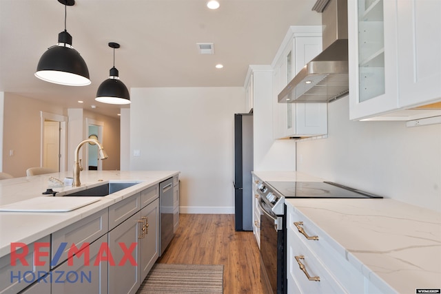 kitchen featuring stainless steel appliances, visible vents, wall chimney range hood, a sink, and decorative light fixtures