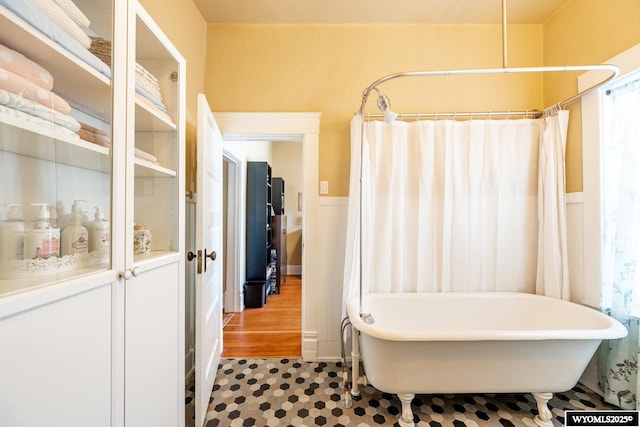 bathroom with a shower with shower curtain, a freestanding tub, and a wainscoted wall