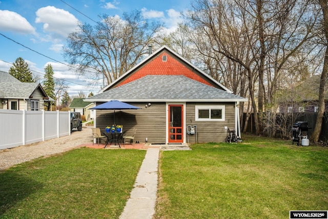 rear view of house with a fenced backyard, roof with shingles, and a lawn
