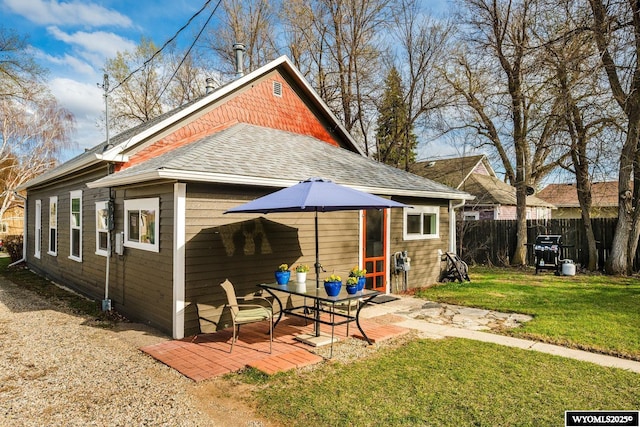 rear view of property with fence, a lawn, roof with shingles, and a patio area