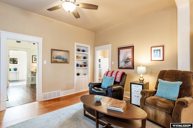 living area with visible vents, a ceiling fan, baseboards, light wood-style flooring, and built in shelves