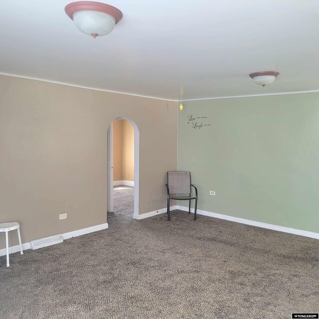 empty room featuring arched walkways, visible vents, carpet floors, and baseboards