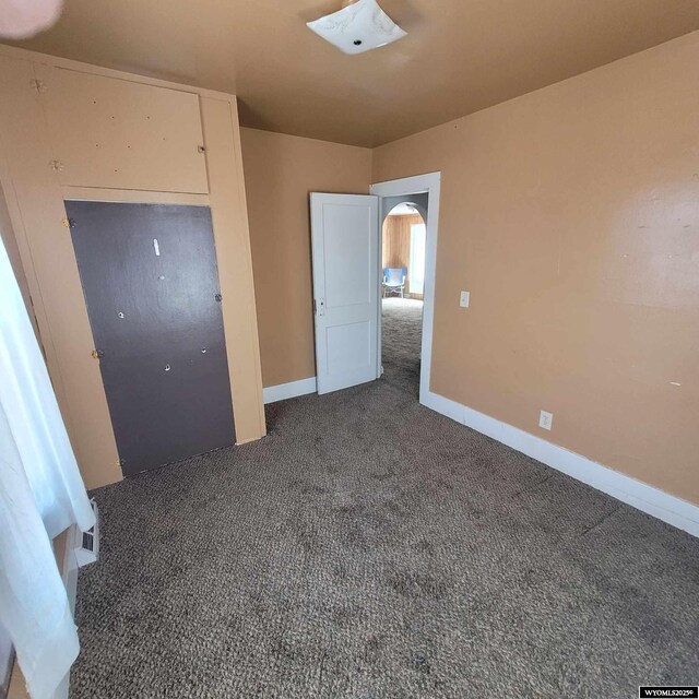 unfurnished bedroom featuring baseboards, carpet flooring, and arched walkways
