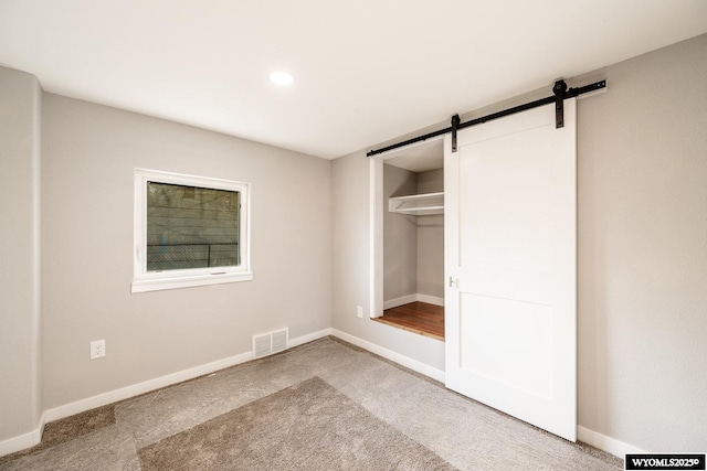 unfurnished bedroom featuring carpet flooring, visible vents, a barn door, baseboards, and recessed lighting