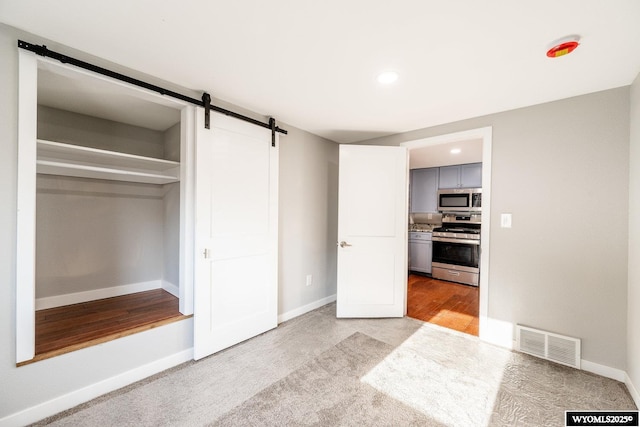 unfurnished bedroom with a barn door, a closet, visible vents, baseboards, and a spacious closet