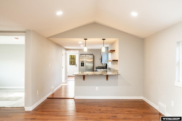 kitchen with wood finished floors, a peninsula, light stone countertops, and stainless steel fridge with ice dispenser