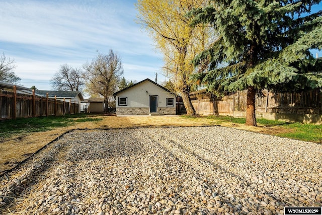 rear view of property featuring stone siding, stucco siding, and fence