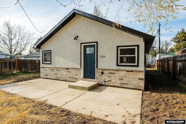 rear view of house with a patio, stone siding, stucco siding, and fence