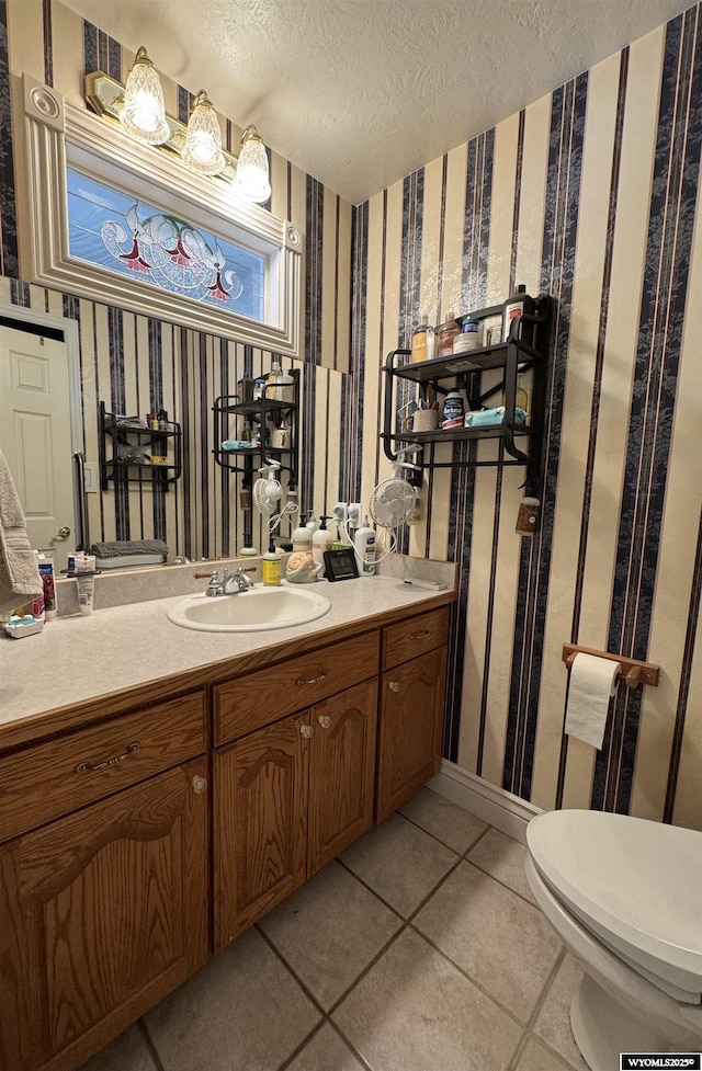 bathroom with tile patterned flooring, wallpapered walls, toilet, vanity, and a textured ceiling