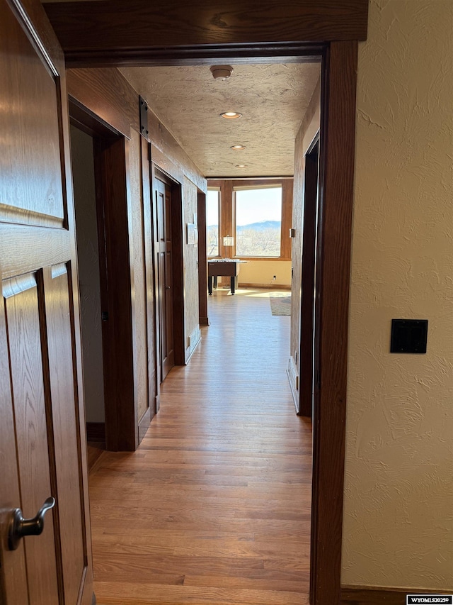 hall with light wood finished floors, a textured wall, and baseboards