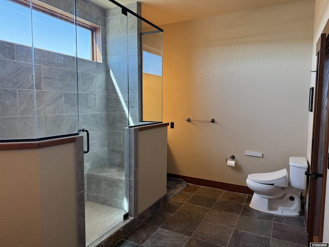 bathroom with baseboards, stone finish flooring, a stall shower, and toilet