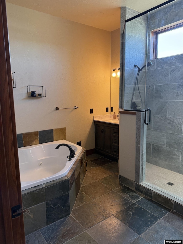bathroom with baseboards, a tub with jets, vanity, stone tile floors, and a stall shower