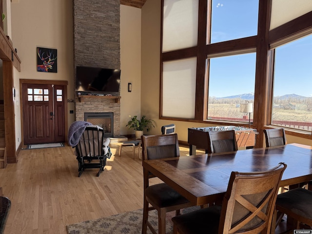 dining space featuring light wood-style floors, a high ceiling, and a stone fireplace