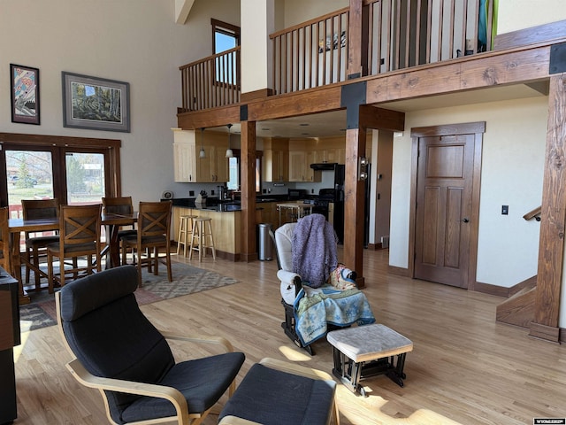 living area featuring a towering ceiling, light wood-style floors, and baseboards