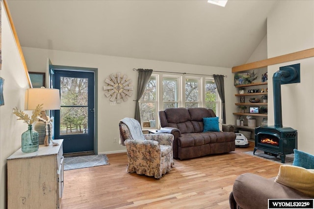 living area featuring a wood stove, a wealth of natural light, light wood-style flooring, and high vaulted ceiling