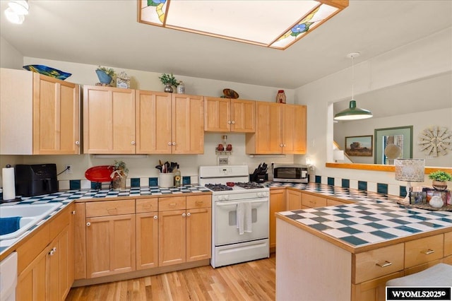kitchen with light brown cabinetry, tile counters, stainless steel microwave, and white range with gas stovetop