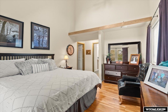 bedroom with light wood finished floors, a towering ceiling, and baseboards