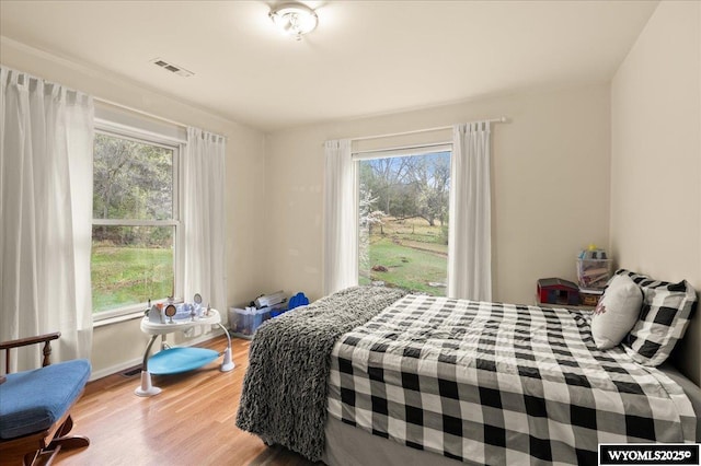bedroom featuring baseboards, visible vents, wood finished floors, and multiple windows