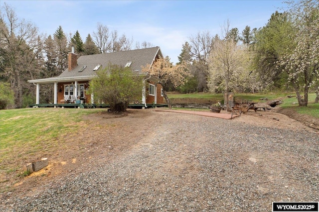 view of front of house with a chimney, a porch, a front yard, and driveway