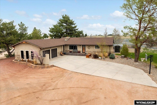 rear view of house featuring driveway, stone siding, an attached garage, and stucco siding