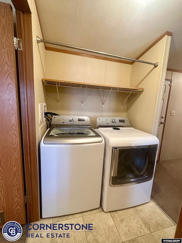 clothes washing area featuring a textured ceiling, washer and dryer, light tile patterned floors, and laundry area