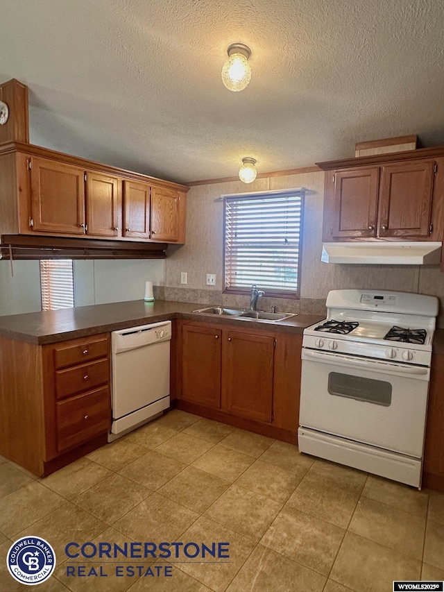 kitchen with white appliances, under cabinet range hood, dark countertops, a sink, and a textured ceiling