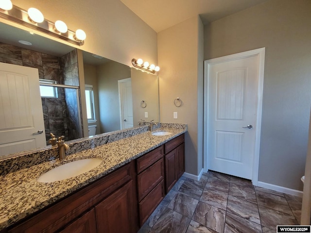 full bathroom with a sink, double vanity, a stall shower, baseboards, and toilet
