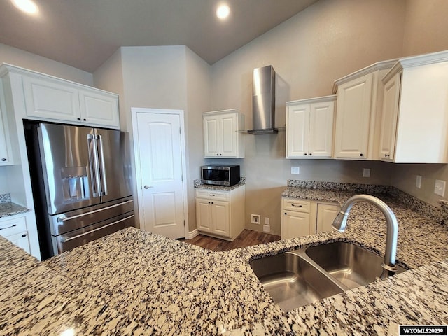 kitchen with wall chimney range hood, a sink, stainless steel appliances, light stone countertops, and wood finished floors