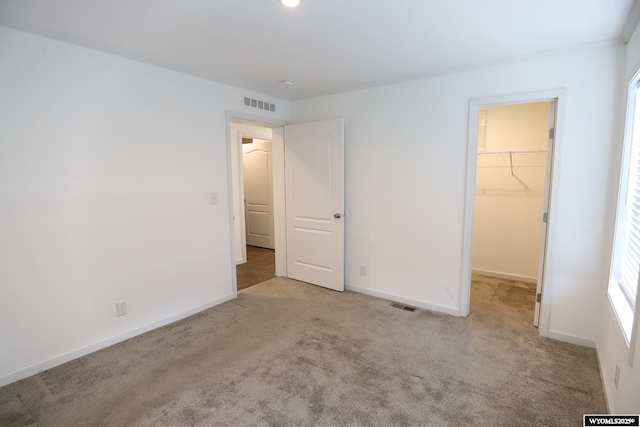 unfurnished bedroom with a walk in closet, carpet, baseboards, visible vents, and a closet