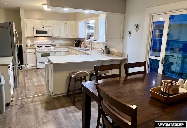 kitchen featuring wood finished floors, a sink, white cabinets, a peninsula, and white appliances