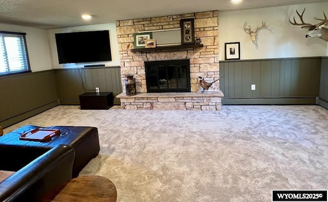living room featuring a stone fireplace, carpet, a baseboard heating unit, and a wainscoted wall
