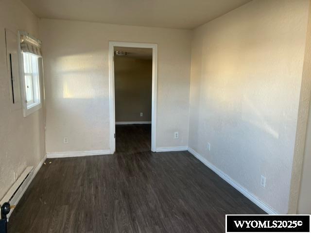 unfurnished room with baseboards, a baseboard radiator, and dark wood-style floors