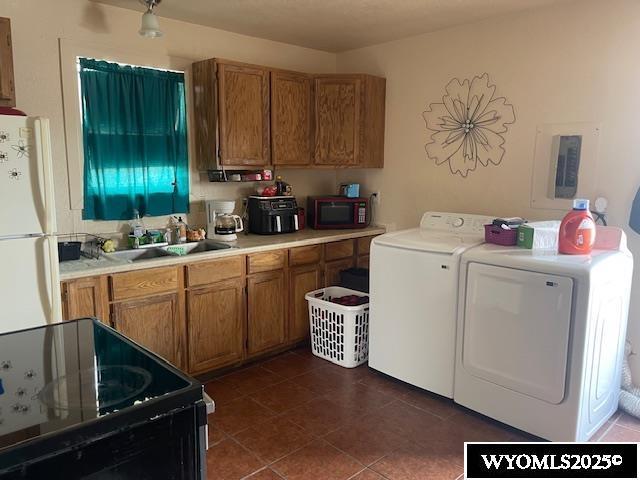 washroom with laundry area, a sink, dark tile patterned floors, washing machine and dryer, and electric panel