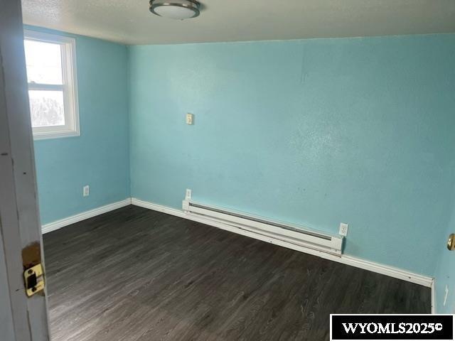 empty room with baseboards, a baseboard radiator, and dark wood-style floors