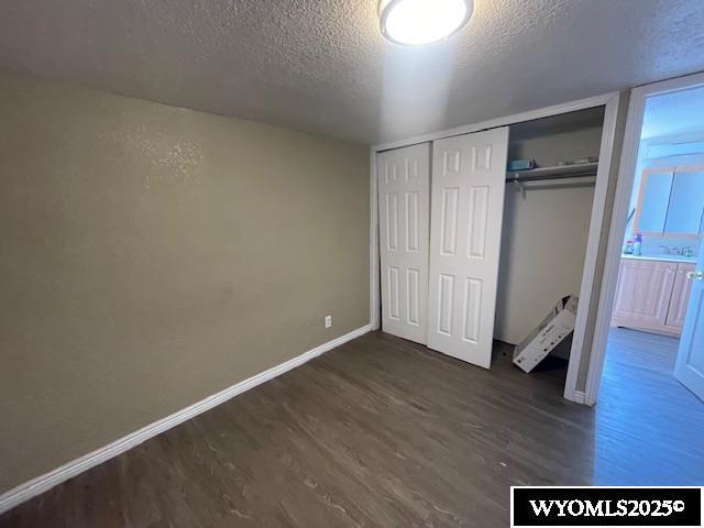 unfurnished bedroom featuring baseboards, a closet, dark wood-style floors, and a textured ceiling
