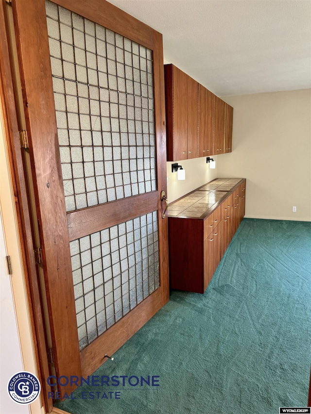 kitchen with carpet flooring, tile counters, and brown cabinetry