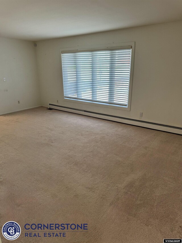 carpeted empty room featuring a baseboard heating unit