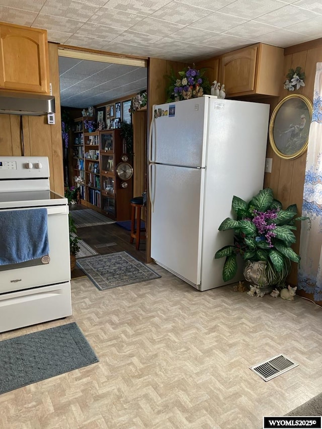 kitchen with white appliances, under cabinet range hood, wood walls, and visible vents