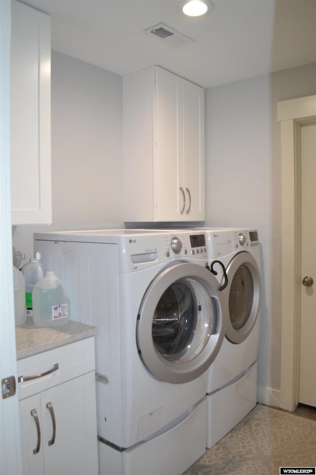washroom with cabinet space, visible vents, and washer and clothes dryer