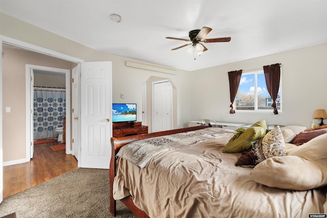 carpeted bedroom featuring arched walkways, a ceiling fan, baseboards, wood finished floors, and a closet