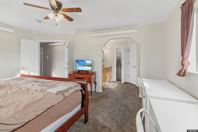 bedroom featuring dark colored carpet, arched walkways, connected bathroom, and ceiling fan