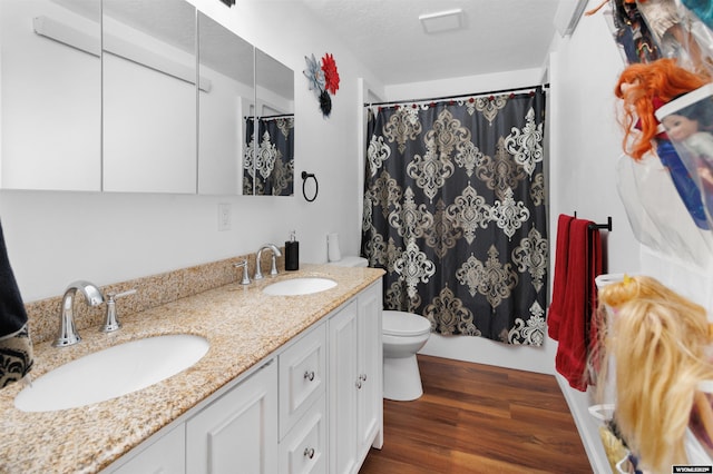 bathroom with a sink, double vanity, toilet, and wood finished floors