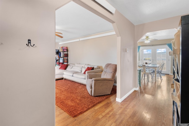 living area with light wood-type flooring, arched walkways, baseboards, and ceiling fan