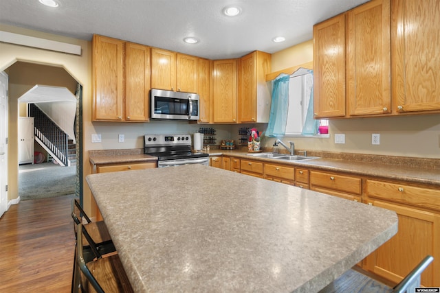 kitchen with a kitchen island, a kitchen bar, dark wood-type flooring, a sink, and stainless steel appliances